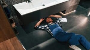 Fixing the siphone. Lying down on the floor. Plumber in blue uniform is at work in the bathroom